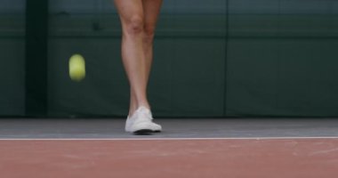 Yakın plan, beyaz spor ayakkabılı genç bir bayan tenisçinin bacakları.