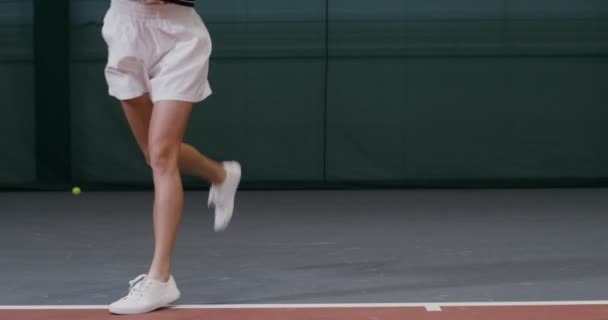 Egy atlétikai egyenruhás nő teniszezik, ugrál, miközben taszítja az ütéseket. — Stock videók
