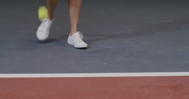 Yakın plan, beyaz spor ayakkabılı genç bir bayan tenisçinin bacakları.