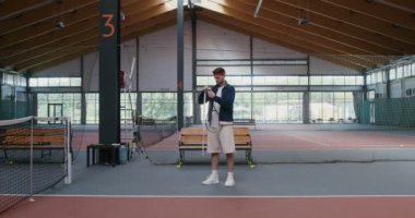 Genç bir adam tenis raketinin sapını özel bir kasetle sarar.
