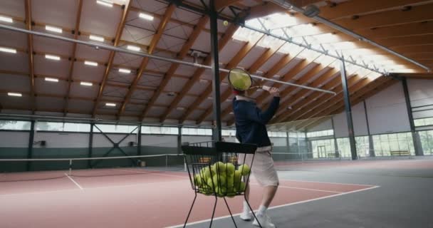 Bir adam tek başına tenis oynuyor, bir sepetten topu alıyor ve bir ağın üzerinden atıyor. — Stok video