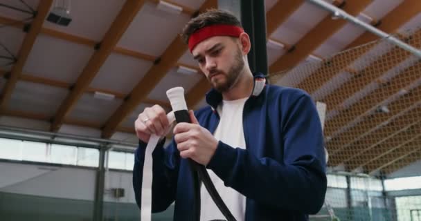 Un giovane avvolge la maniglia di una racchetta da tennis con un nastro speciale — Video Stock