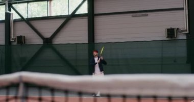 Bir adam büyük tenis oynar, topa raketle tekrar tekrar vurur.
