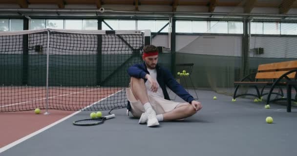 Egy férfi pihen edzés után, miközben a háta egy teniszhálón pihen. — Stock videók
