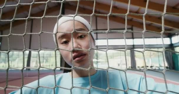 Pemain tenis wanita muda melihat kamera melalui jaring tenis — Stok Video