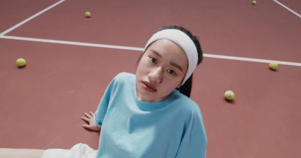 Жінка сидить на підлозі в тенісному корті і дивиться на камеру без посмішки — стокове відео