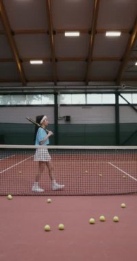 Tenis raketi olan bir kadın tenisçi tenis ağına yaslanmış poz veriyor.
