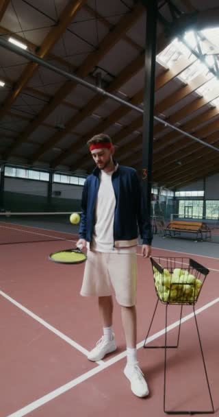 Um jovem enche uma bola de tênis com uma raquete, vídeo vertical — Vídeo de Stock