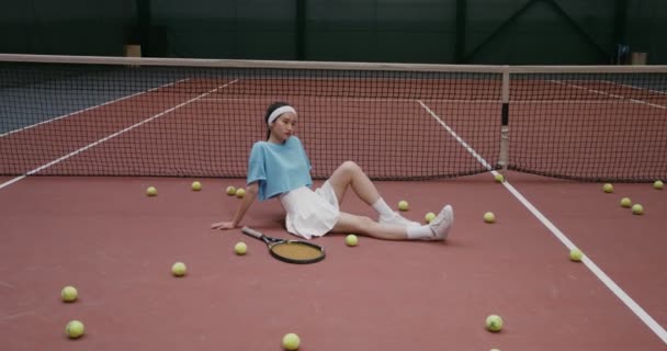 Jugadora de tenis sentada en el suelo de una pista de tenis y mirando a la cámara — Vídeos de Stock