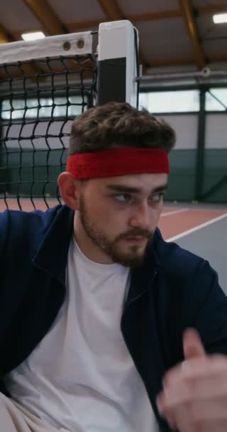 Een man rust na een training met zijn rug rustend op een tennisnet — Stockvideo