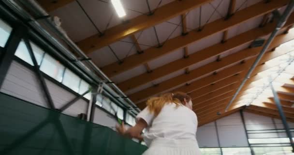 Mujer joven juega al tenis en una cancha de tenis cubierta, golpeando la pelota con una raqueta — Vídeo de stock
