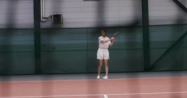 Bir kadın tenisçi tenis oynar, topa tekrar tekrar vurur.