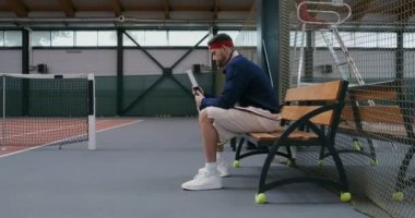 Genç bir adam tenis raketinin sapını özel bir kasetle sarar.