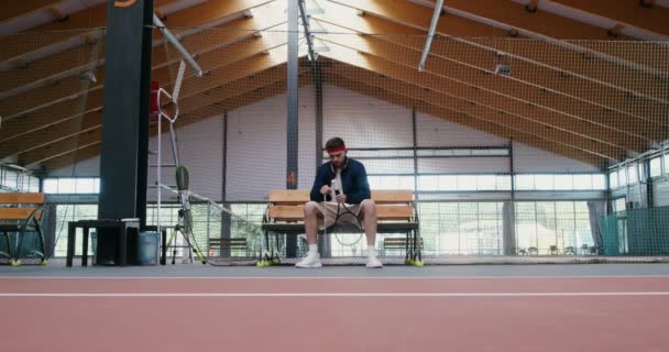 Ein junger Mann wickelt den Griff eines Tennisschlägers mit einem speziellen Klebeband — Stockvideo