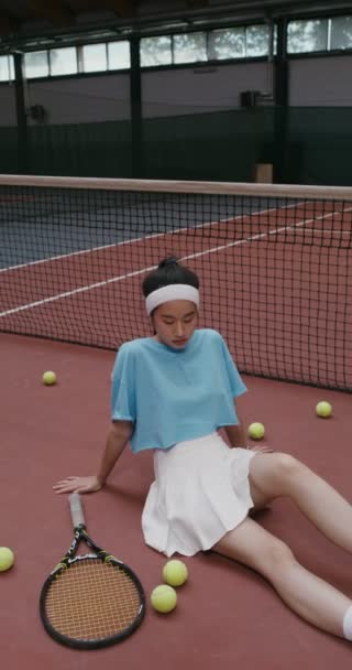 Γυναίκα τενίστρια κάθεται στο πάτωμα ενός γηπέδου τένις και κοιτάζει την κάμερα — Αρχείο Βίντεο