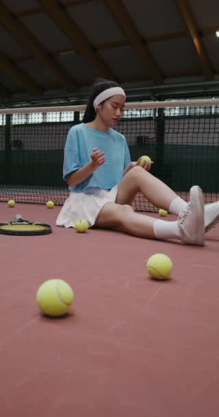 Тенісист сидить на підлозі тенісного корту кидає м'яч з рук в руки — стокове відео