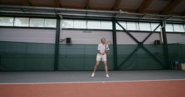 Genç bir kadın tenis kortunda tenis oynuyor, raketle topa vuruyor.