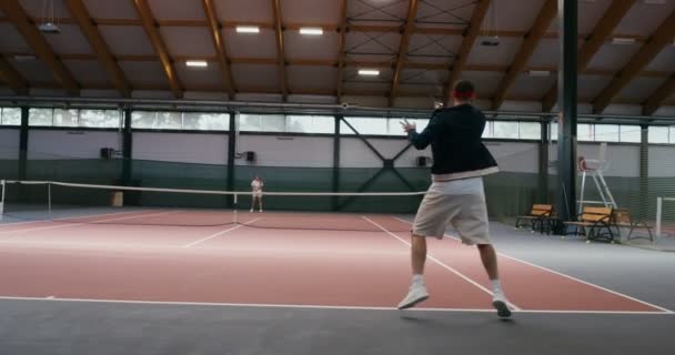 Ung man och kvinna spelar tennis på inomhus tennisbana, slå slag efter slag — Stockvideo