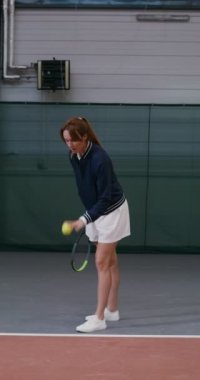 Bir kadın tenis maçına topu fırlatarak ve raketle vurarak başlar.