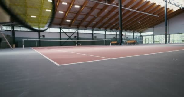Um homem carrega uma cesta cheia de bolas de tênis e uma raquete de tênis em suas mãos — Vídeo de Stock