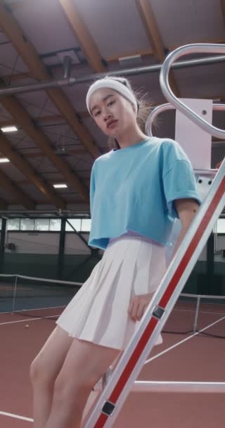 Uma mulher tenista senta-se nas escadas da cadeira de árbitros e olha para a câmera — Vídeo de Stock