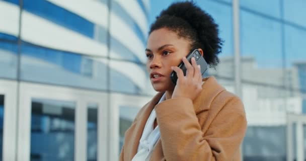 Egy afro-amerikai nő, aki mobilon beszél, és komolyan néz a szabadban. — Stock videók