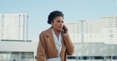 Afro-Amerikalı bir kadın cep telefonuyla konuşuyor. Dışarıya ciddi bir şekilde bakıyor.