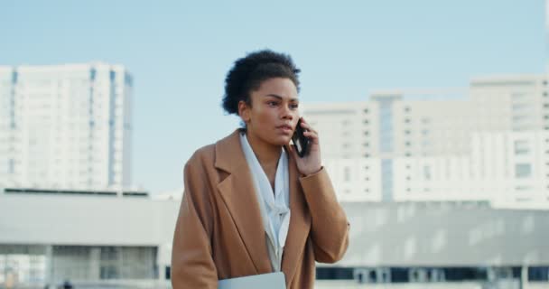 Африканская американка разговаривает по мобильному телефону с серьезным видом на улицу — стоковое видео
