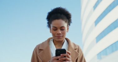 Dışarıda cep telefonu kullanırken gülümseyen Afro-Amerikalı bir iş kadını.