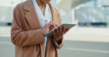 Afro-Amerikalı kadın dışarıda dururken tablet kullanırken gülümsüyor.