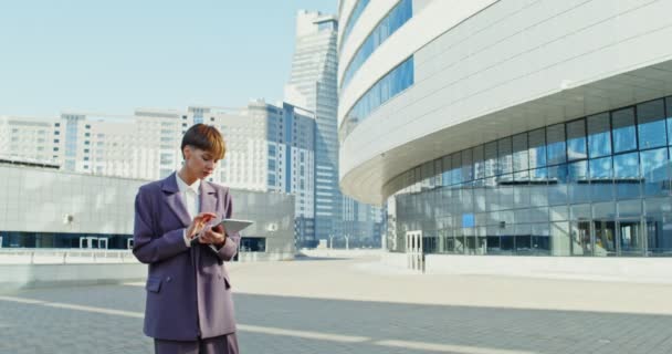 Une femme vêtue d'un costume d'affaires utilise une tablette qui touche l'écran, à l'extérieur — Video