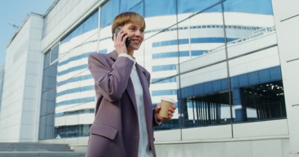 スーツを着た女性が携帯電話で話し街を歩くコーヒーを飲んで — ストック動画