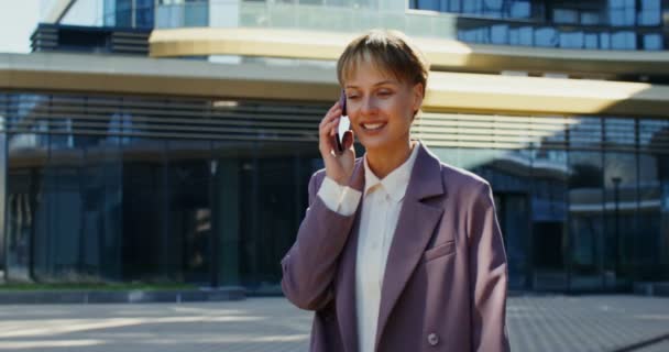 Молодая женщина в современном деловом костюме разговаривает по мобильному телефону на улице — стоковое видео