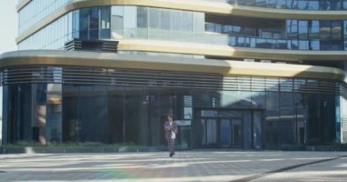 Bir kadın caddede modern bir iş merkezinin yanında yürüyor ve tablet kullanıyor.