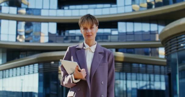 Une femme d'affaires regarde directement dans la caméra tout en se tenant près de l'immeuble de bureaux — Video