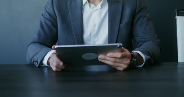 Um homem usa um tablet enquanto se senta em uma mesa no escritório, close-up — Vídeo de Stock