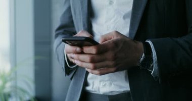 Takım elbiseli genç bir adam cep telefonuyla yazı yazıyor, yakın plan.