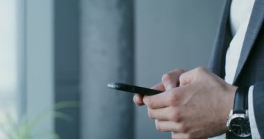 Takım elbiseli genç bir adam cep telefonuyla yazı yazıyor, yakın plan.