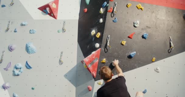 Um jovem sobe a parede de escalada interior sem cordas de segurança — Vídeo de Stock