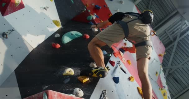 Un joven equipado con arneses de escalada baja por la pared de escalada — Vídeo de stock