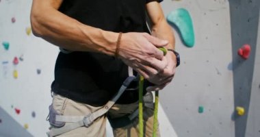 Bir adam tırmanma duvarının önünde dururken emniyet kemeri takıyor.