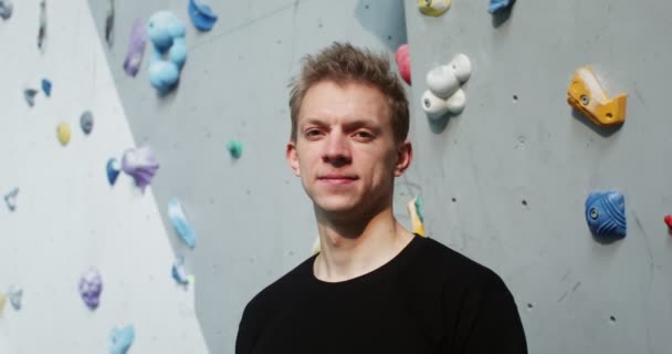A young man looks straight into the camera standing in front of climbing wall — Stock Video