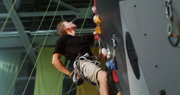 Un hombre con un cinturón de seguridad trepando por la pared de escalada — Vídeos de Stock