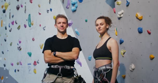 Jovem homem e mulher olhando para a câmera de pé na frente da parede de escalada — Vídeo de Stock