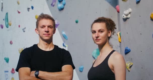 Mladý muž a žena se dívají do kamery stojící před lezeckou stěnou — Stock video