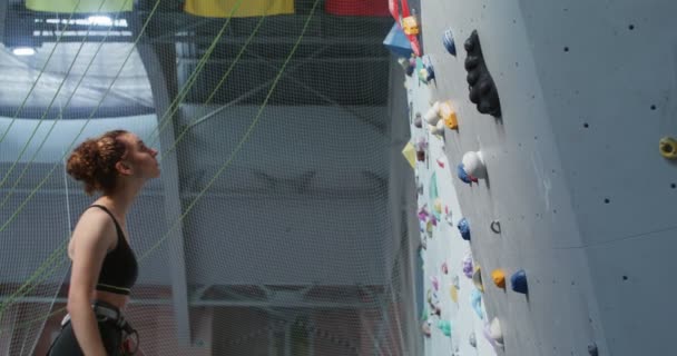 Jovem atleta olha para cima enquanto está em frente a uma parede de escalada — Vídeo de Stock