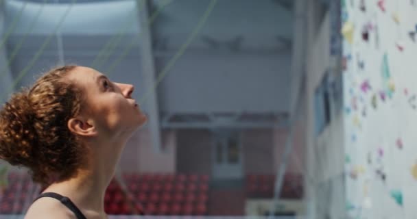 Joven mujer comienza a subir la pared de escalada agarrando piedras artificiales — Vídeos de Stock