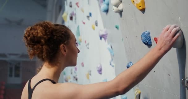 Jovem mulher começa a subir a parede de escalada agarrando em pedras artificiais — Vídeo de Stock