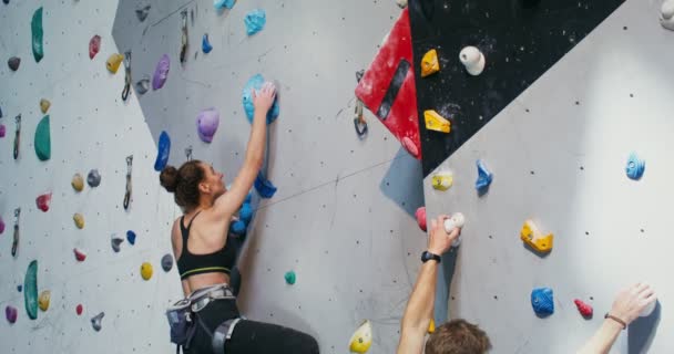 Una joven pareja trepa por el muro de escalada, agarrando piedras artificiales — Vídeos de Stock