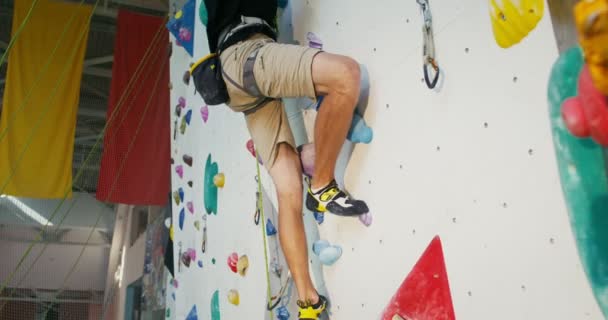 Un hombre se dedica a escalar en roca sobre una superficie artificial en una pared de escalada — Vídeos de Stock